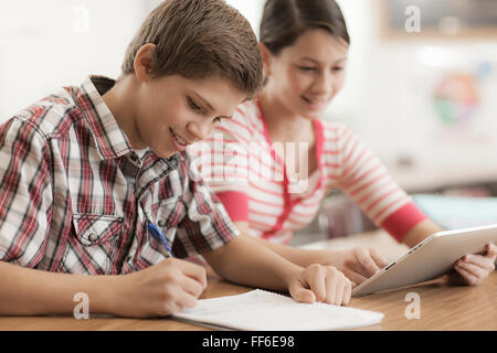 Two children, a boy and girl sitting in class, sharing a digital tablet. Stock Photo