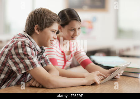 Two children, a boy and girl sitting in class, sharing a digital tablet. Stock Photo