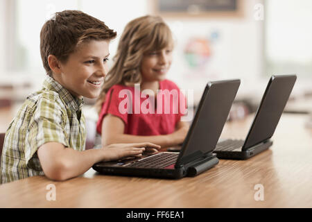 Two children seated at desks in class using laptop computers. Stock Photo