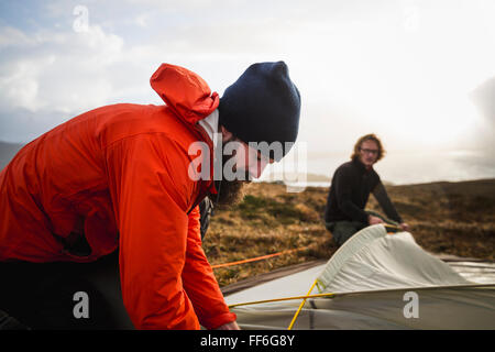 Two men holding and putting up a small tent in open space. Wild camping. Stock Photo