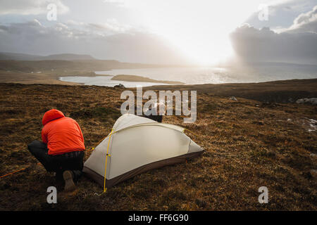 Two men holding and putting up a small tent in open space. Wild camping. Stock Photo