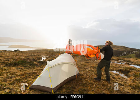 Two men holding and putting up a small tent in open space. Wild camping. Stock Photo