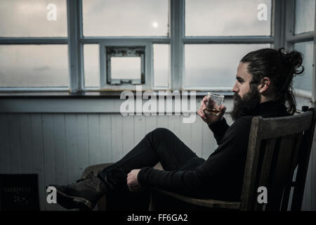 A man sitting looking at the view out of a window, drinking from a glass. Stock Photo