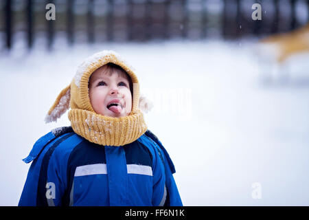 Sweet little boy, catching snowflakes in the park, playground, wintertime Stock Photo