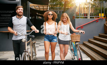 Three young people walking down the street with their bicycles. Male and female friends on road with their bike. Stock Photo