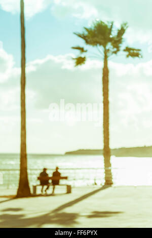 blurred picture of  elder couple sitting on a bench in a mediterranean setting facing the sea Stock Photo