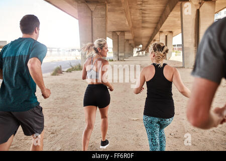 Group of young people working out in the city. Young men and women running under a bridge. Stock Photo