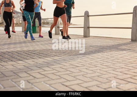 Low section cropped shot of people running on street by the sea. Fitness group training on seaside promenade. Stock Photo