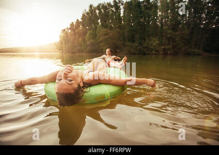 Portrait of smiling young girl floating in an innertube with a man at the background in a lake. Young couple in lake on inflatab Stock Photo