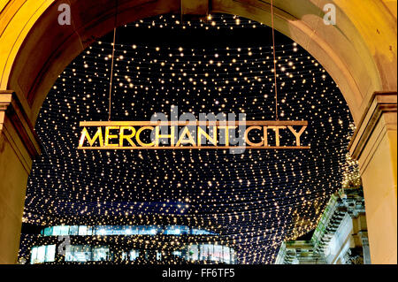 The Merchant City sign in Royal Exchange Square, Glasgow city centre, lit up at night against a twinkling backdrop. Stock Photo