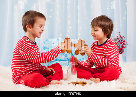 Two happy children eating cookies at christmas and drinking milk, laughing and talking, having fun Stock Photo