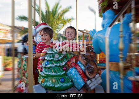 Sweet boys, brothers, riding in a Santa Claus sledge on a merry-go-round, carousel attraction in Europe, active children, summer
