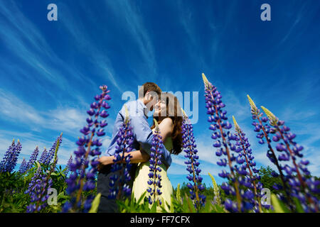 Couple in lupine flowers field embracing and smiling Stock Photo