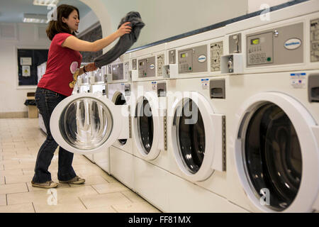 A young British woman loads clothes into a washing machine in a launderette in Wadebridge, Cornwall, UK. The energy for the launderette is sourced from roof solar panels and is part of a scheme to make this town the first to be powered by renewable sources in the UK. Stock Photo