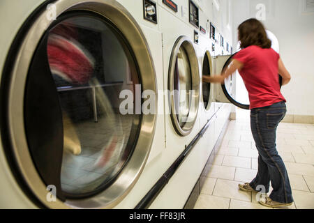 A young British woman loads clothes into a washing machine in a launderette in Wadebridge, Cornwall, UK. The energy for the launderette is sourced from roof solar panels and is part of a scheme to make this town the first to be powered by renewable sources in the UK. Stock Photo