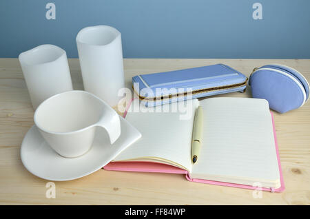 White cup, elegant notepad, pen, blue leather wallet and purse on wooden table with blue wall behind Stock Photo