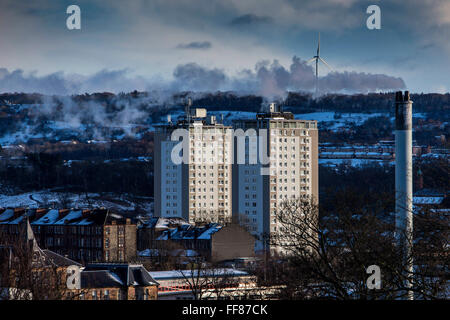 Two blocks of flats, a smoking chimney and a wind turbine on Glasgow South side taken from Queens Park, Glasgow. Stock Photo