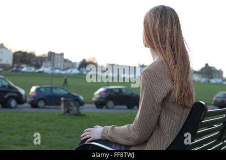 Young pensive woman sitting on a bench looking into the distance. Stock Photo