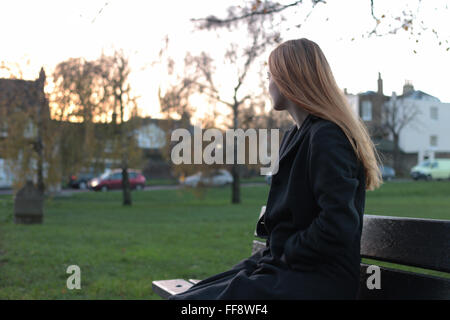 Young pensive woman sitting on a bench looking into the distance. Stock Photo