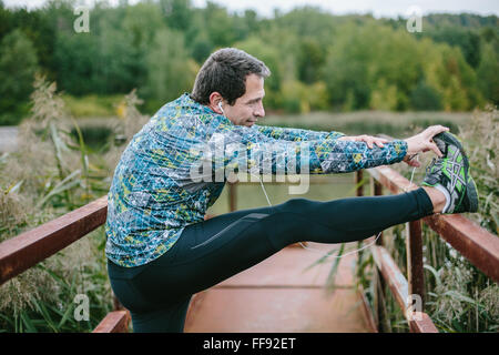 Runner on rusty bridge stretching against green nature Stock Photo