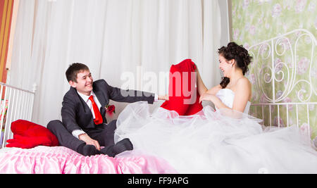 Portrait of happy newlywed couple fighting with pillows in bed Stock Photo