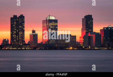 A beautiful sunset over the skyscrapers of Jersey City and the Hudson River, with the pink sky reflected in the water.