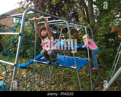 Two Girls Sisters On Climbing Frame One Girl On Monkey Bars In Garden England Stock Photo