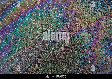 Colorful oil sheen, caused by oil leaking from a vehicle, on wet