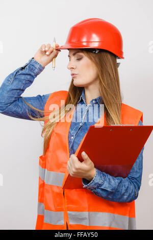Woman construction worker builder structural engineerin in orange vest red hard helmet holds pen file pad. Safety in industrial Stock Photo