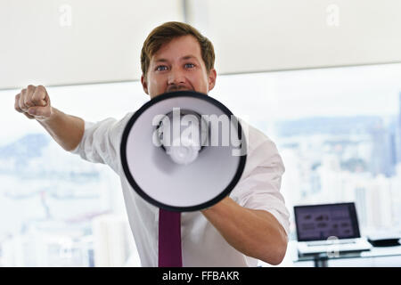Angry businessman with megaphone in modern office looking at camera. The angry man screams and fights for his labor rights. Stock Photo