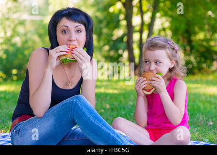 Mom and daughter eating tasty burgers on a picnic Stock Photo