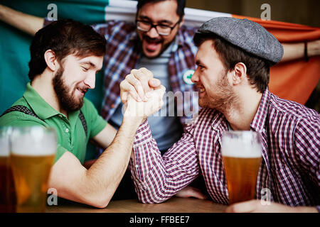 Two strong young men arm-wrestling in pub Stock Photo
