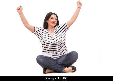 Successful casual woman sitting with legs crossed and raising her fists isolated on white background Stock Photo