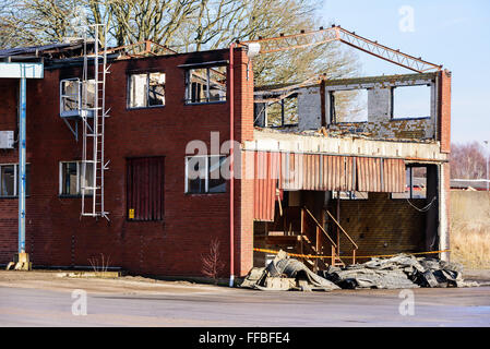 A small industrial building has burnt down. The roof is gone and some of the metal roof beams has been bent by the heat. Stock Photo