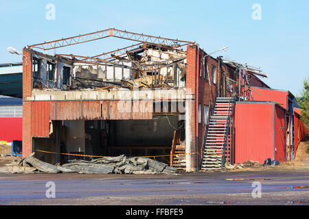 A small industrial building has burnt down. The roof is gone and some of the metal roof beams has been bent by the heat. Stock Photo