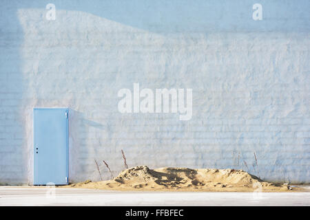 A cemented brick wall background with a metal door without handle in the corner and a pile of sand in front. Copy space on wall. Stock Photo