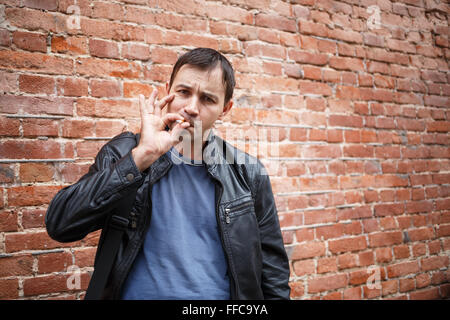 Man smoker in the background of an old brick wall. Bully in the alley. Smoking bad boy. Stock Photo