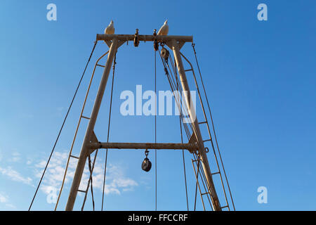 Fragment of an old fishing boat mast with ropes and winches with seagulls sitting on it against the blue sky. Stock Photo
