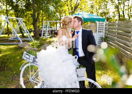 Pretty young bride and groom with retro bike in a green park Stock Photo