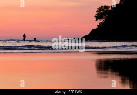 Two people standing in the sea at sunset off a beach in western Sabah, Malaysia Stock Photo