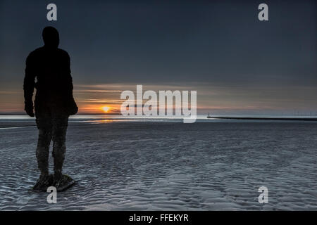 The iron men statues of Antony Gormley's Another Place on Crosby beach look out towards Liverpool Bay at sunset Stock Photo