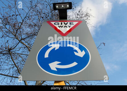 british road sign indicating a roundabout ahead and instructing road users to give way on reaching it Stock Photo