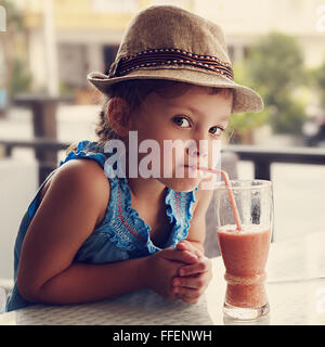 Curious fun cute kid girl in hat drinking tasty juice in summer street cafe. Closeup toned portrait Stock Photo