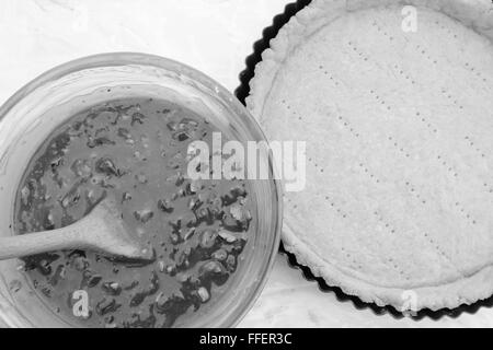 Making pecan pie - nutty pie filling ready to pour into the blind-baked pie crust - monochrome processing Stock Photo