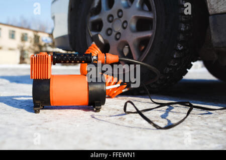 Car air compressor in working position at snow. Self-inflating wheels, automobile tire pressure control. Stock Photo