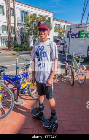 A male teenager stops and pauses his ride on his  hoverboard on a sidewalk in Santa Barbara, California wearing sunglasses. Stock Photo