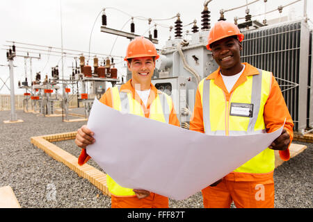 smiling electricians holding blueprint at substation Stock Photo