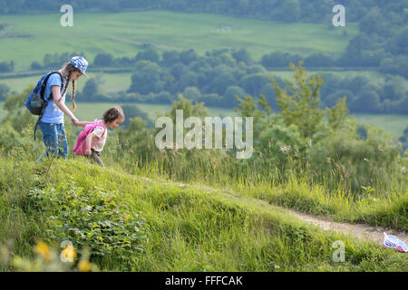 Sisters holding hands in the english countryside. A younger sister leads her sibling by the hand with views over farmland Stock Photo