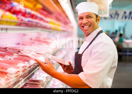 mid age butcher organizing meat products in butchery Stock Photo