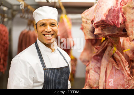 happy butcher standing in cold room with beef hanging Stock Photo